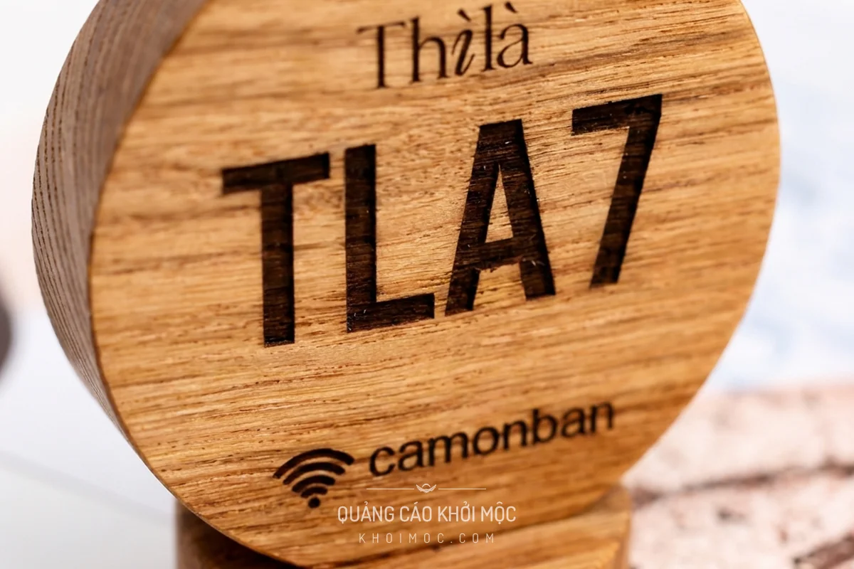 Ảnh macro nghệ thuật thẻ gỗ tròn, logo Thìlà và mã TLA7 khắc laser